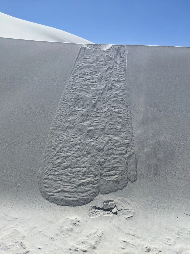 A sharp-crested gypsum dune at White Sands with wind-blown sand streaming from its ridge.